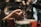 Hands are shown preparing a coffee machine for use, with a portafilter being inserted into an espresso machine. The background has a blurred appearance, focusing on the action of making coffee.