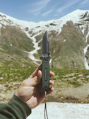 Close-up of hands holding a handcrafted, practical outdoor tool against a mountain backdrop.