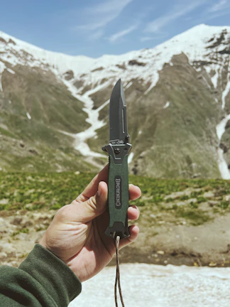 Close-up of hands holding a handcrafted, practical outdoor tool against a mountain backdrop.