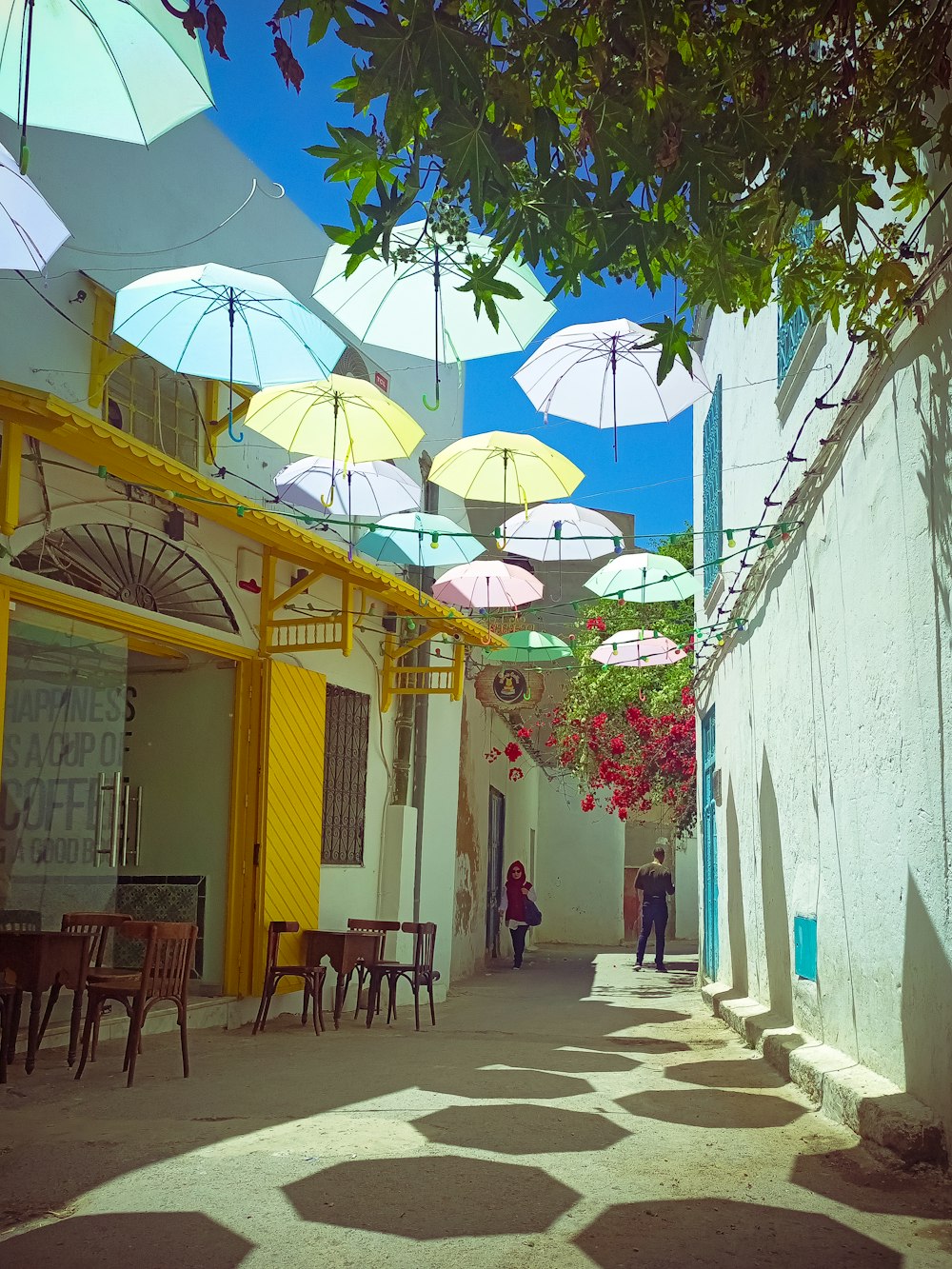 a narrow street with tables and umbrellas hanging from the ceiling