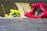 A vibrant yellow inflatable rescue boat appears to be partially submerged in front of a dam's spillway, with water cascading down the structure. Nearby, a pink rescue craft with multiple people on board is heading towards the scene, suggesting an active rescue operation on a flowing river.