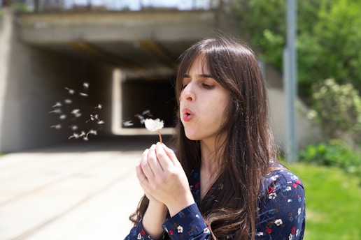 a woman blowing a dandelion with her hands
