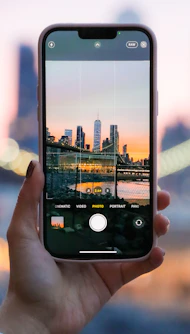 A vibrant sunrise over a cityscape with a traveler checking their budget app on a smartphone.