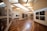 A modern art gallery with wooden flooring and neutral-colored walls, displaying black and white photographs in sleek frames along the walls. The space is well-lit with a combination of natural light from skylights and ceiling-mounted lighting fixtures.