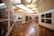 A modern art gallery with wooden flooring and neutral-colored walls, displaying black and white photographs in sleek frames along the walls. The space is well-lit with a combination of natural light from skylights and ceiling-mounted lighting fixtures.