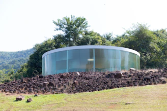 a round glass building on a hill with trees in the background