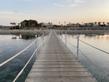 A wooden pier stretching into the calm, crystal-clear waters of Trincomalee beach at sunrise.