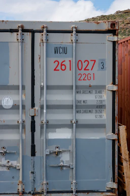 A close-up of a 20-foot shipping container door with rust textures under soft sunlight.