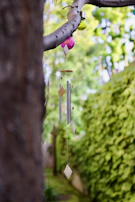 An outdoor wind chime made of weathered metal tubes hanging gently from a wooden beam, with a blurred garden background.
