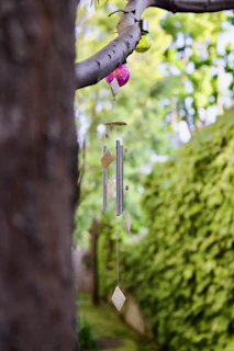 An outdoor wind chime made of weathered metal tubes hanging gently from a wooden beam, with a blurred garden background.