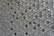 A pattern of countless hexagonal tiles creating a geometric texture. These tiles have a three-dimensional appearance with varying shades of grey and hints of subtle reflections, giving them a metallic or ceramic look.