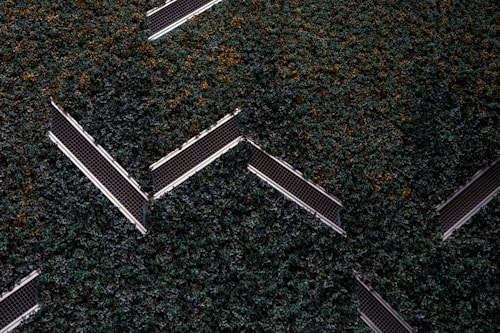 Aerial view of a series of solar panels embedded within dense green foliage, arranged in a geometric zigzag pattern.