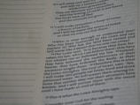 A close-up of a page from a book displaying text in columns. The page is slightly curled and features a mixture of prose and poetry. The left side shows a margin with dotted lines, and the text includes use of italics and bold type for emphasis.