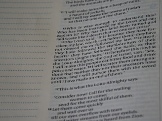 A close-up of a page from a religious text, featuring numbered verses and passages written in two columns. The text is printed in a serif font on off-white paper with faint grey lines separating sections.