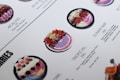 A close-up of a menu displaying various smoothie bowls. The bowls are placed in rows with descriptions and calorie counts next to each. The bowls are decorated with fresh fruits like strawberries, blueberries, and exotic fruits. The design and layout are clean with a white background and aesthetically pleasing presentation.