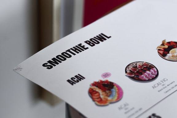 The image features part of a menu highlighting smoothie bowls, with a focus on terms like 'SMOOTHIE BOWL' and 'ACAI'. There are small images of different kinds of smoothie bowls with colorful fruit and toppings.