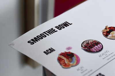 The image features part of a menu highlighting smoothie bowls, with a focus on terms like 'SMOOTHIE BOWL' and 'ACAI'. There are small images of different kinds of smoothie bowls with colorful fruit and toppings.