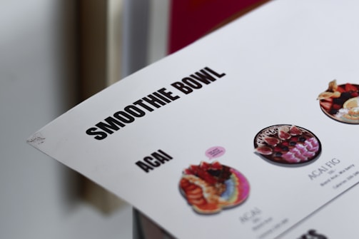 The image features part of a menu highlighting smoothie bowls, with a focus on terms like 'SMOOTHIE BOWL' and 'ACAI'. There are small images of different kinds of smoothie bowls with colorful fruit and toppings.