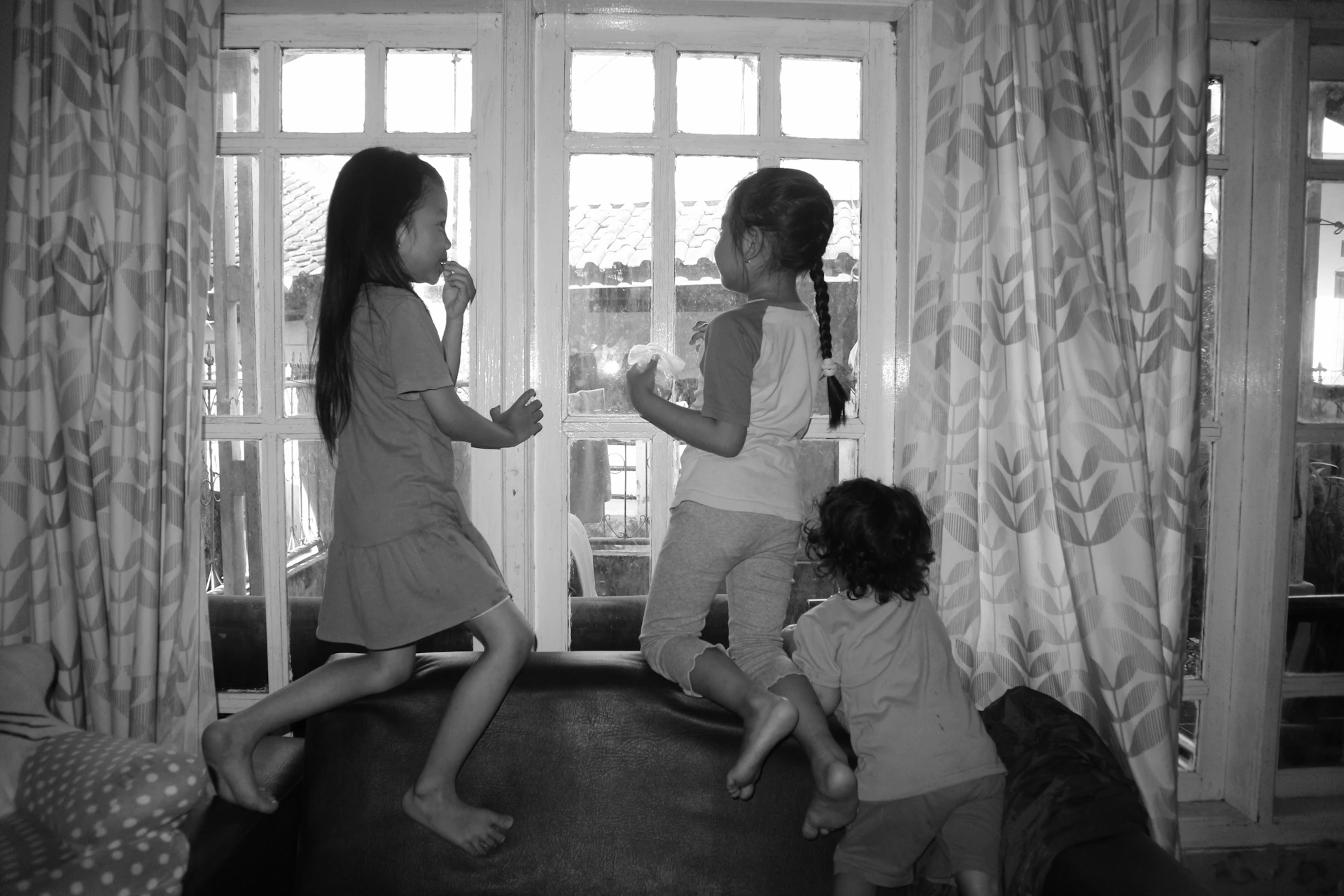 A cheerful nanny playing with children in a bright, comfortable living room filled with natural light.