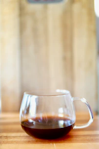 A steaming cup of freshly brewed coffee on a wooden table with sunlight filtering through nearby windows.