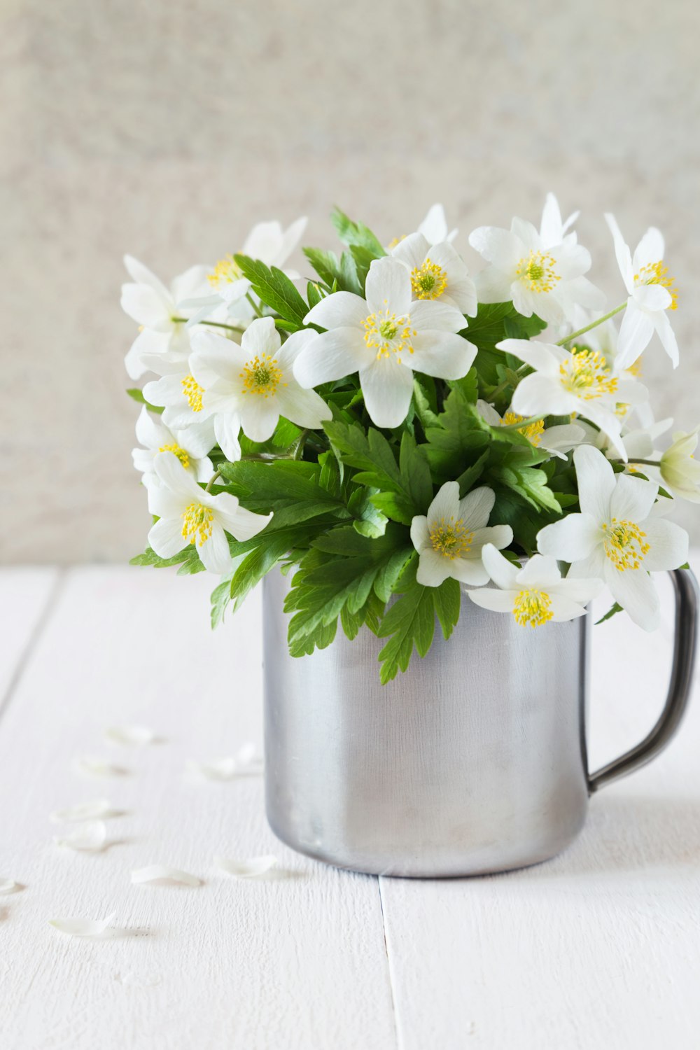 a metal mug filled with white flowers on top of a table