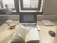 A workspace with a laptop displaying a document, an open book, a lamp, a glass of coffee, and a book titled 'Atomic Habits' on a wooden desk. Sunlight is coming through a window, casting natural light over the setup.