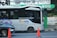 A modern public bus is parked at a bus stop with its side adorned by decorative purple graphics. The bus displays the hashtag '#PilihanCerdasBermobilitas' and is branded with 'BIS-KITA.' In front of the bus, an orange traffic cone is visible. The bus stop is marked by a green and black sign with logos. The background includes a wall with street art and graffiti.