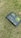A solar charge controller is placed on grass, featuring a green and black design with various icons and text indicating its functionality. The device includes symbols for solar panels, battery, and other power-related functions.
