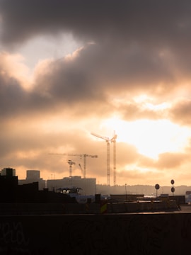 Construction site of a sophisticated urban development with cranes and scaffolding under a moody charcoal sky.