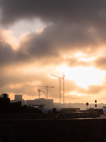 A panoramic view of a bustling construction site with cranes lifting steel beams under a dramatic Afghan sky.