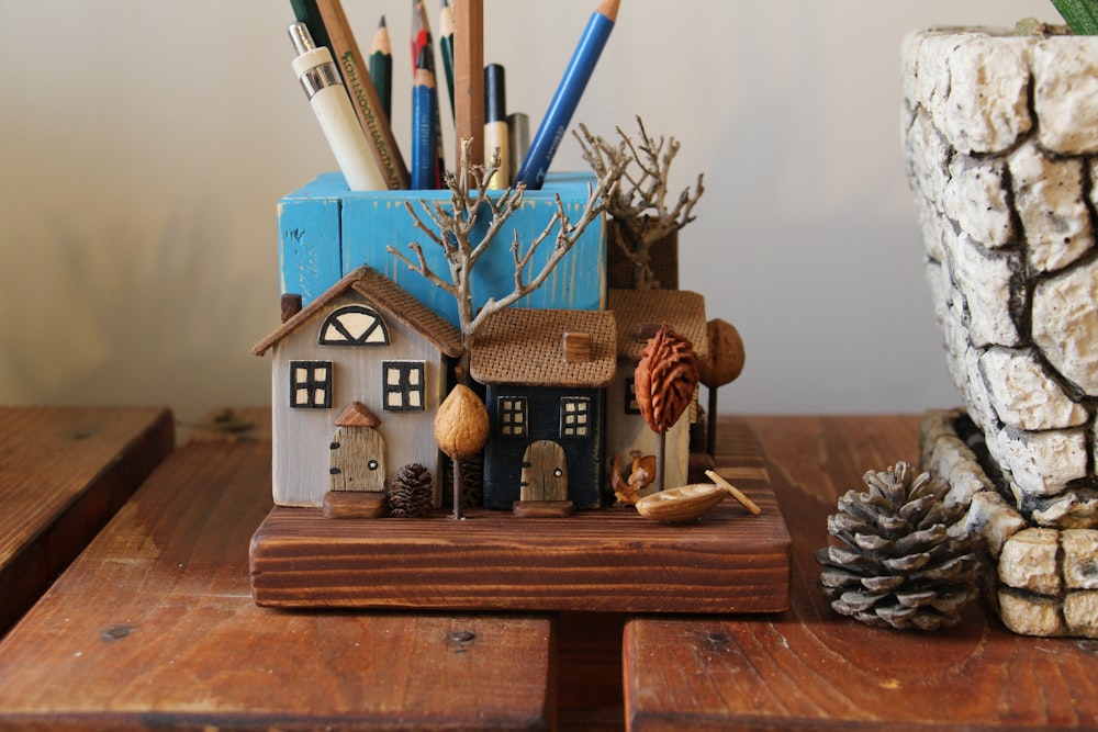 a wooden table topped with a small house next to a pine cone