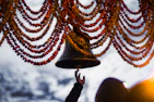 Hands holding a traditional bell above an altar decorated with flowers and holy books.