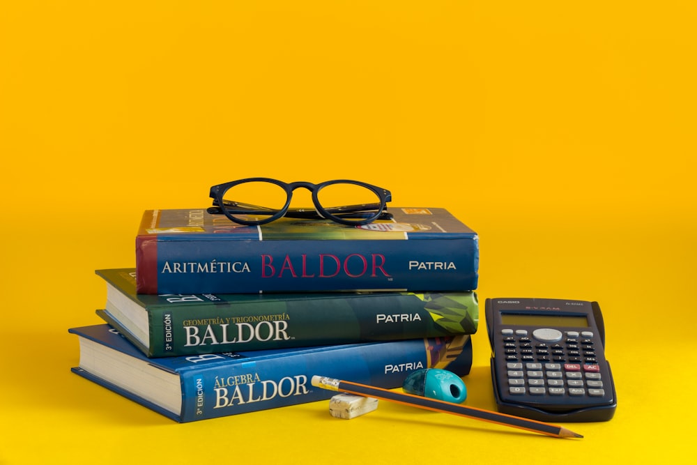 a stack of books and a calculator on a yellow background