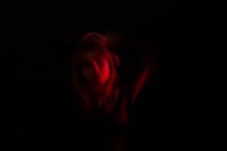 A person is partially illuminated with red light against a dark background. The lighting creates a dramatic and mysterious atmosphere with soft, blurred edges.