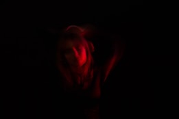 A person is partially illuminated with red light against a dark background. The lighting creates a dramatic and mysterious atmosphere with soft, blurred edges.