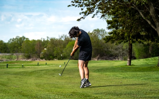 A golfer swinging a club on a lush green golf course under a clear blue sky.