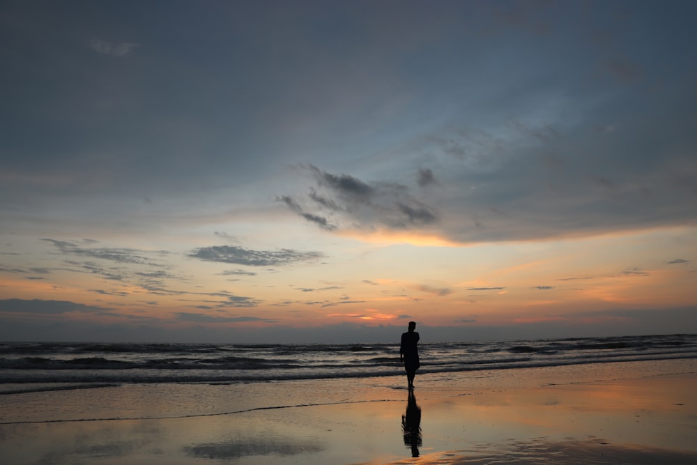 uma pessoa em pé em uma praia ao pôr do sol