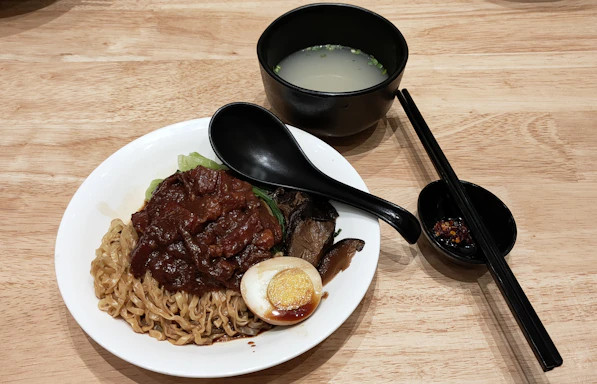 A rustic wooden table with bowls of steaming broth-based dishes surrounded by fresh herbs and vegetables.