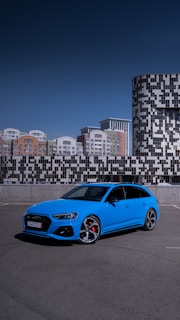 A blue compact car parked in front of a modern urban building.