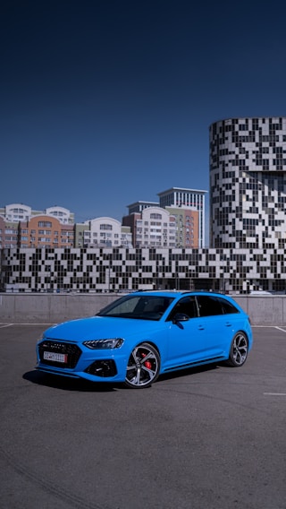 A bright blue modern driving school car parked on a sunny street with a clear sky.