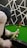 A person is poised to take a shot on a green snooker or pool table. The player, seen from behind, holds a cue stick aimed at several colored balls on the table. The background features a geometric black and white pattern, adding an artistic touch to the scene.