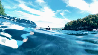 Swimmer cutting through deep blue ocean water with rocky arch in background under clear sky