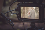 A natural scene showing a couple interacting with a sleek digital prototype, light filtering through trees.