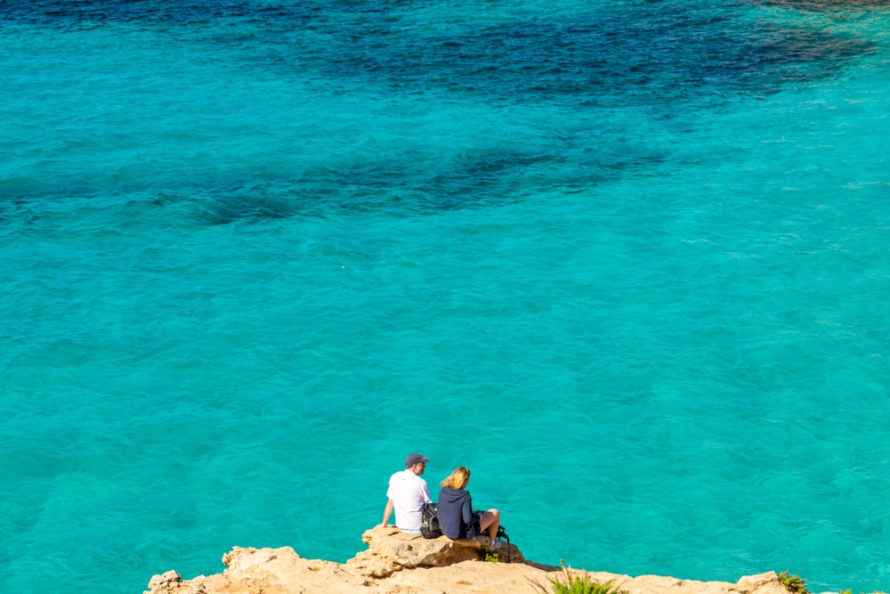 a couple of people sitting on top of a rock near the ocean