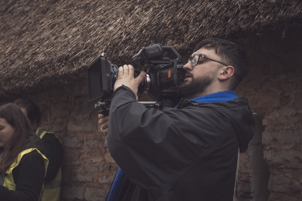 a man holding a camera in front of a thatched roof