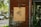 A wooden sign with the text 'FEED FACTORY' and a Chinese character is mounted on a weathered, rust-colored metal wall. The background features parked cars and green trees, creating a blend of urban and natural elements.