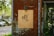 A wooden sign with the text 'FEED FACTORY' and a Chinese character is mounted on a weathered, rust-colored metal wall. The background features parked cars and green trees, creating a blend of urban and natural elements.