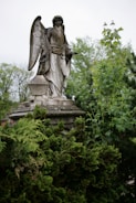 Elegant concrete angel statue standing gracefully beside a garden bench.