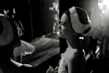 Ballet dancers are preparing backstage, with one prominently featured woman in a stage costume and headpiece. Soft lighting highlights their expressions of calm concentration.