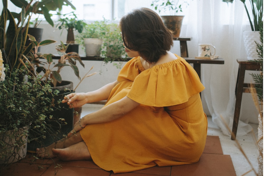 a woman in a yellow dress sitting on the floor next to a potted plant